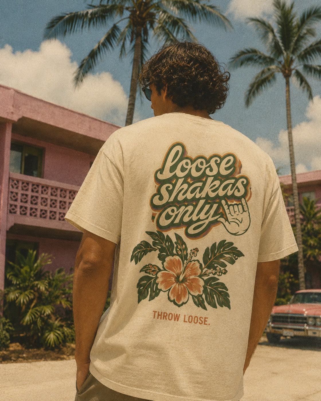 Back of the Loose Shakas Only tee outside a pink Waikīkī apartment block
